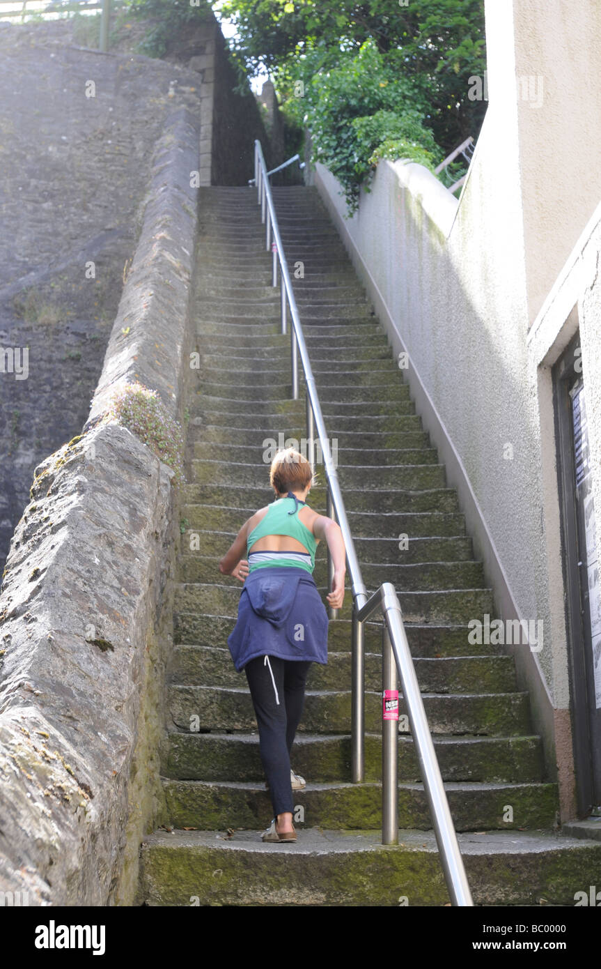 A 40 anno vecchia donna si arrampica su di una ripida scalinata in pietra in Falmouth, Cornwall, Regno Unito mentre una vecchia signora scende. Foto Stock