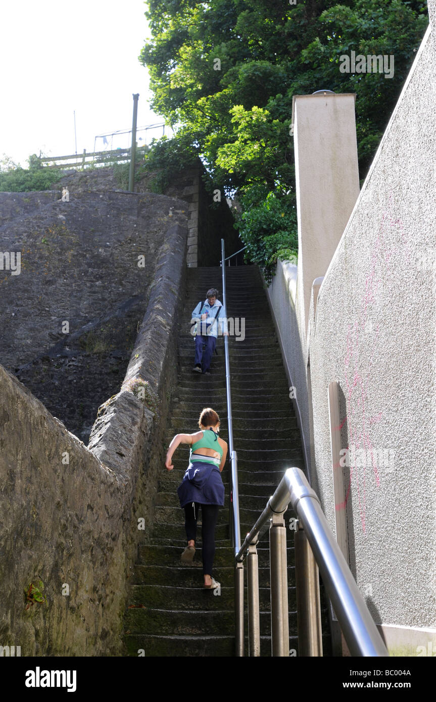 A 40 anno vecchia donna si arrampica su di una ripida scalinata in pietra in Falmouth, Cornwall, Regno Unito mentre una vecchia signora scende. Foto Stock