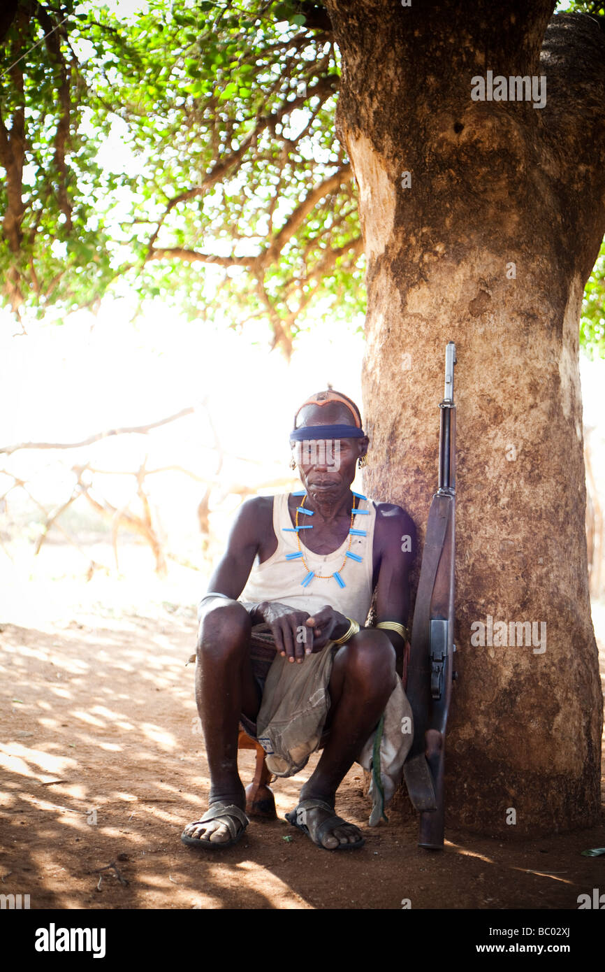 Un uomo dal villaggio Hamer si siede vicino ad un albero con il suo fucile Kalashnikov accanto a lui. Foto Stock
