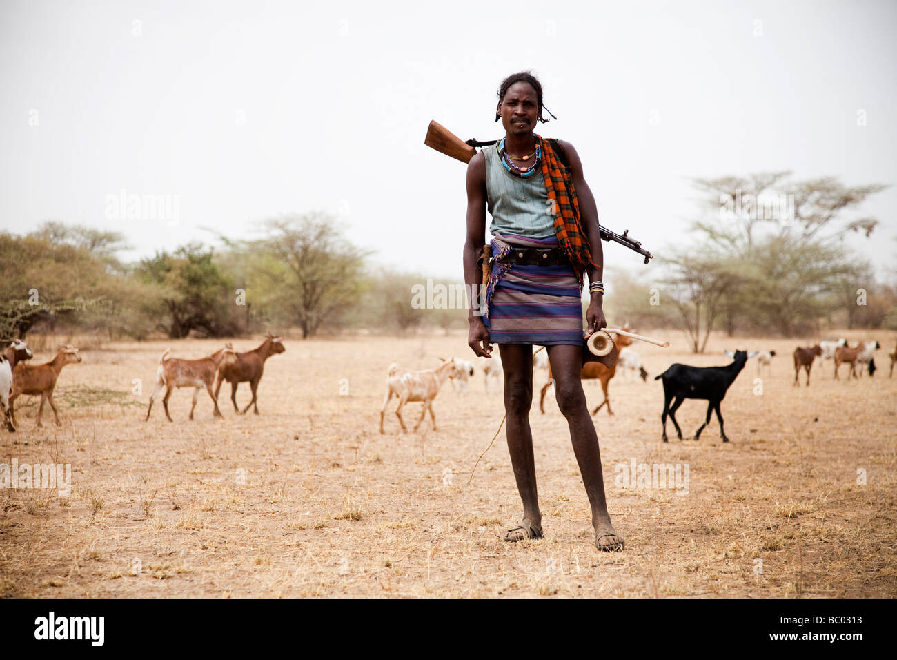 Una capra herder spinge la sua mandria attraverso il deserto nel sud dell Etiopia con un fucile sulla schiena. Foto Stock