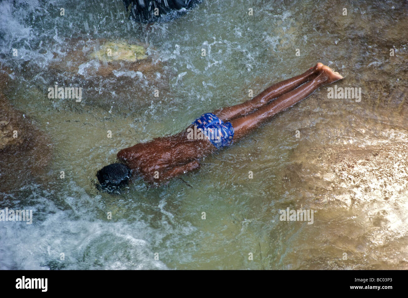 Un giovane ragazzo sommerge se stesso a faccia in giù in una piscina di acqua al di sotto di una cascata durante un festival voodoo in Haiti. Foto Stock