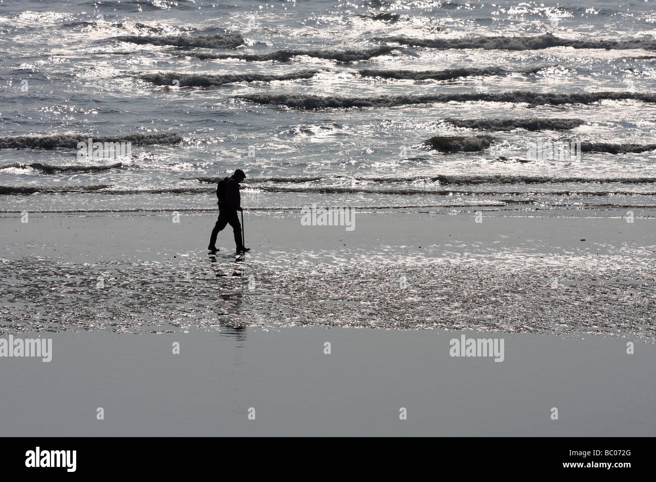 Uomo a camminare sulla spiaggia bagnata in silhouette. Foto Stock