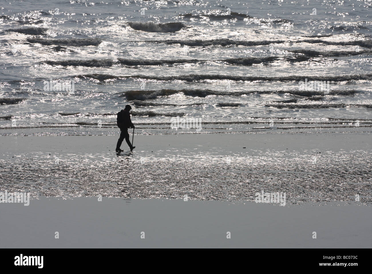 Uomo a camminare sulla spiaggia bagnata in silhouette. Foto Stock