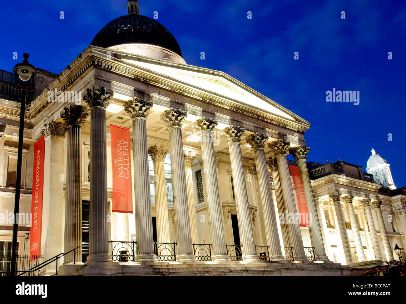 National Gallery illuminata in stile neoclassico Portico Night Londra Regno Unito | LONDRA, Regno Unito — il portico neoclassico illuminato della National Gallery si affaccia su Trafalgar Square di notte, con le sue colonne scanalate che si innalzano su un frontone con il nome del museo. L'architetto William Wilkins completò l'edificio principale nel 1838, riutilizzando le colonne recuperate dalla demolita Carlton House, un tempo residenza di re Giorgio IV Foto Stock
