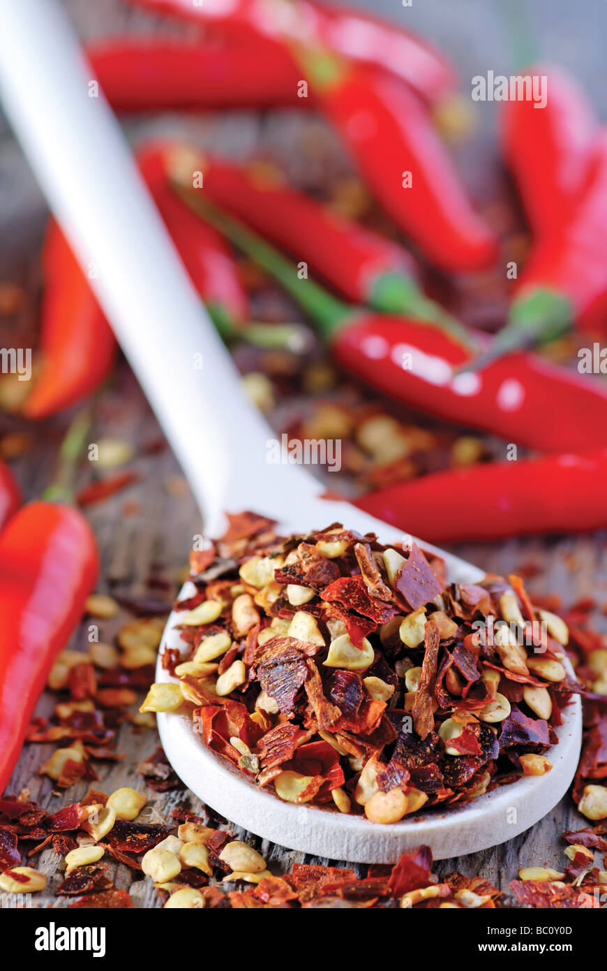 Chiusura del cucchiaio colma di peperoncino sbriciolato scaglie con peperoncino rosso in background Foto Stock