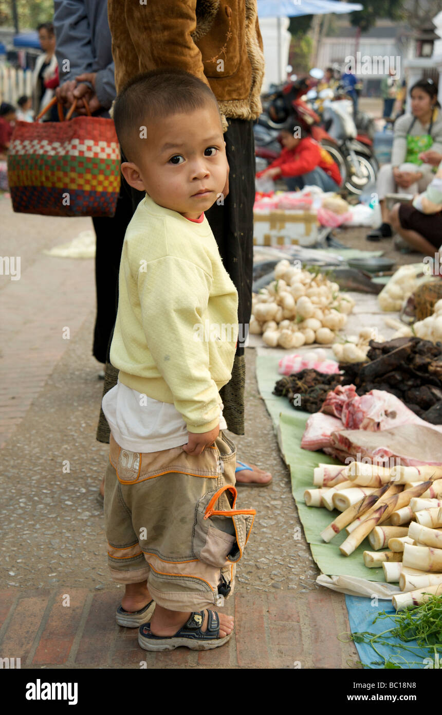 Un giovane ragazzo di Lao trattiene la sua mano le madri in Luang Prabang è fresco giornaliero mercato alimentare Foto Stock