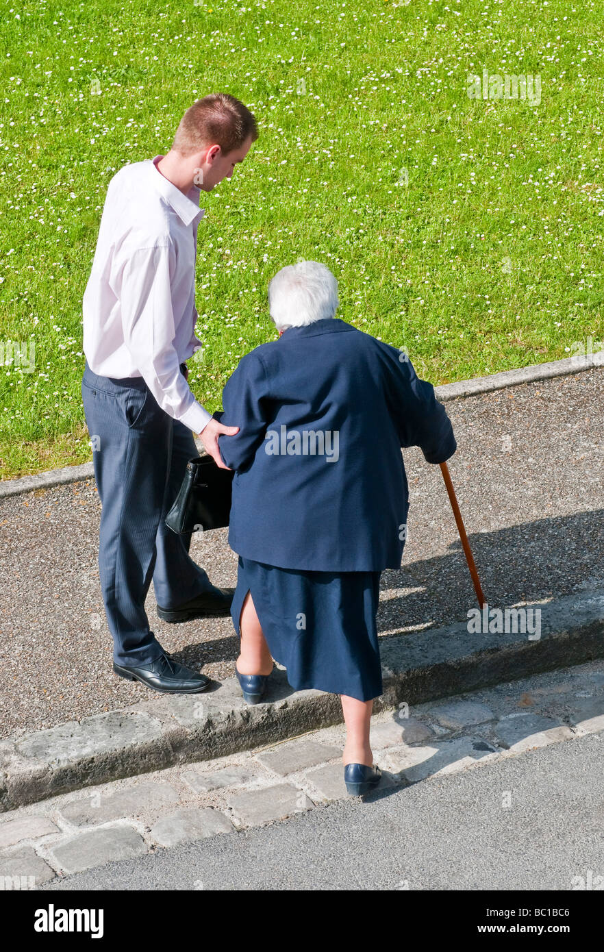 Giovane uomo aiutando donna anziana sul marciapiede - Francia. Foto Stock