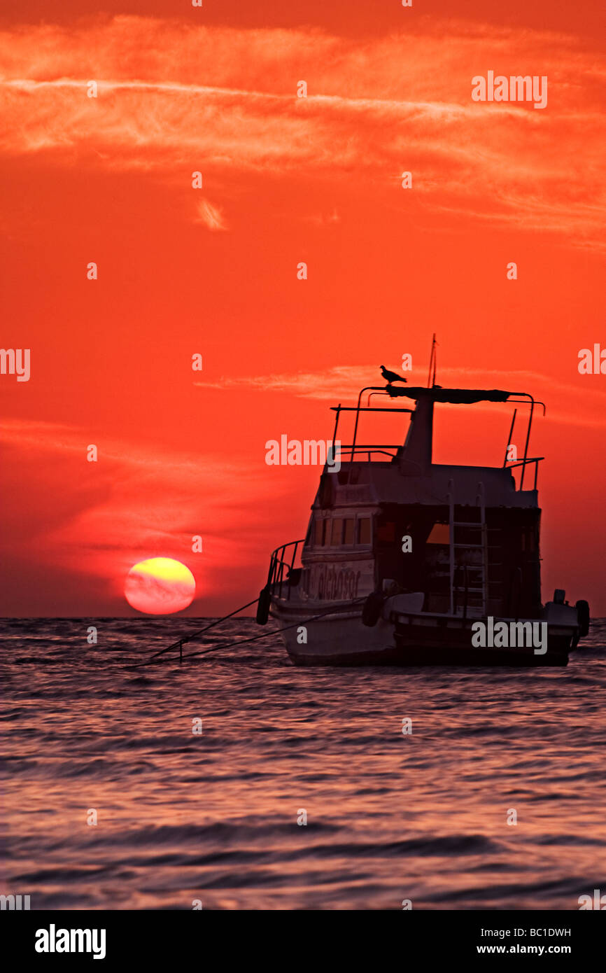 Sun dipping verso un mare tropicale dietro la silhouette di una barca Foto Stock