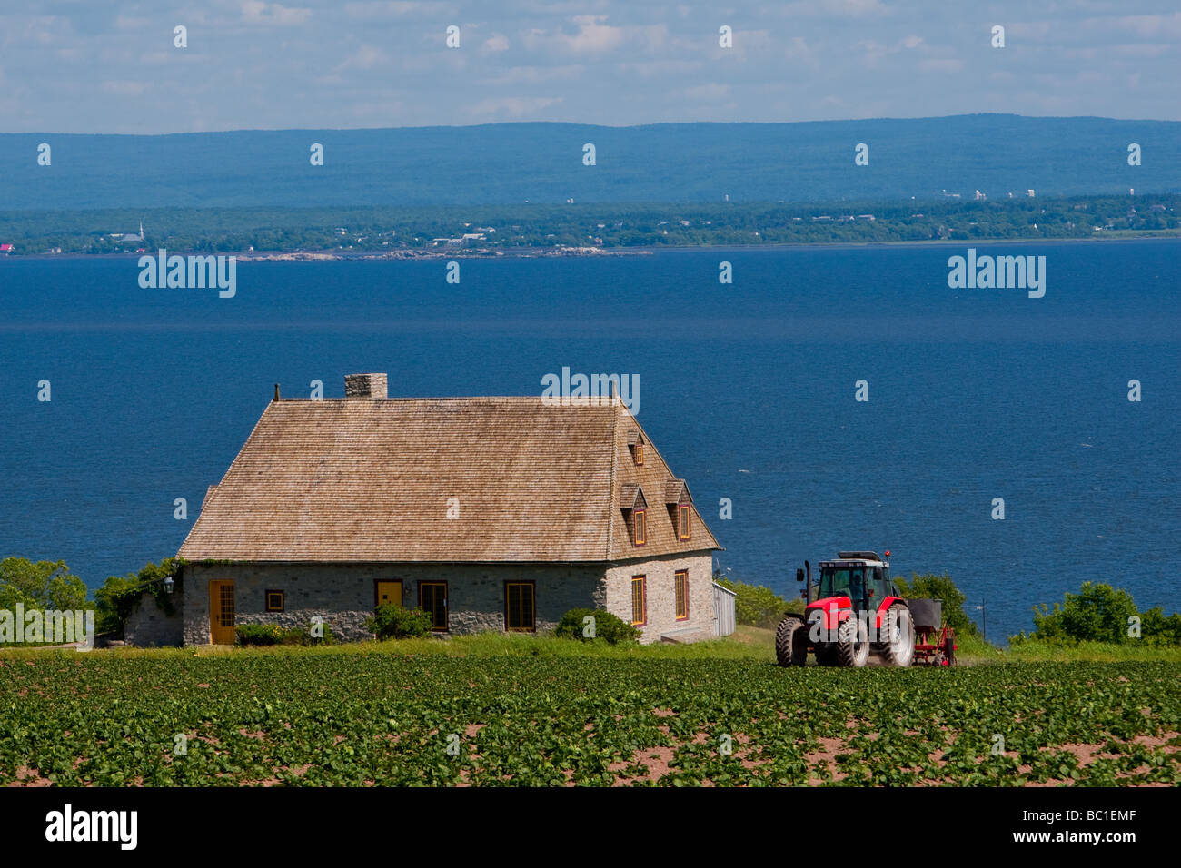 Un agricoltore cavalca il suo trattore sul suo campo nella parte anteriore di uno stile della Normandia house di Saint Jean de l'Ile d'Orleans, Quebec, Canada Foto Stock