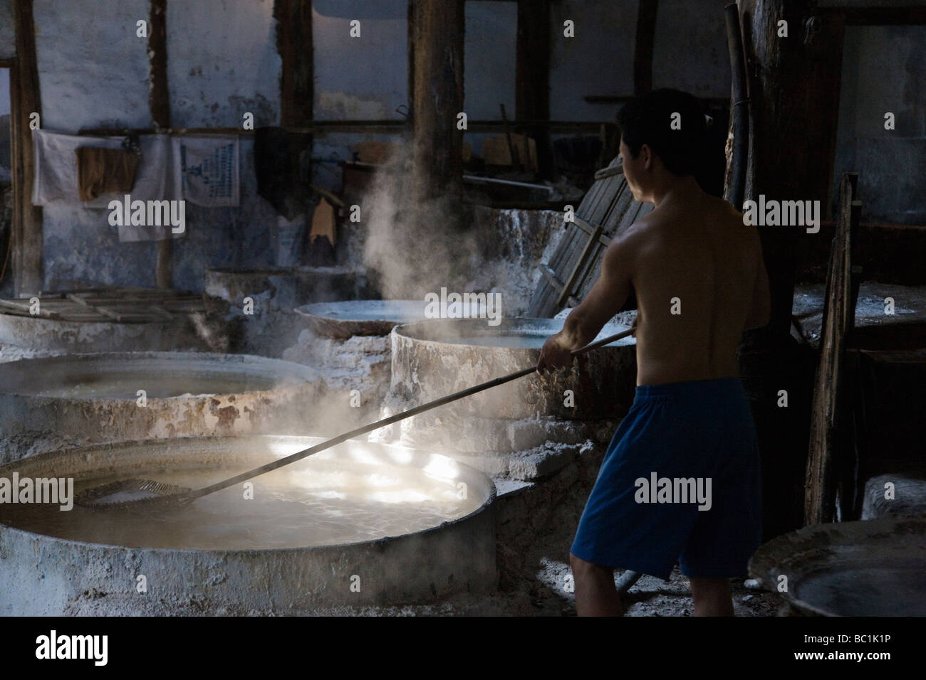 L'uomo in laboratorio utilizzando il modo tradizionale per estrarre il sale dalla salamoia satura di acqua con il sale Zigong Cina Sichuan Foto Stock