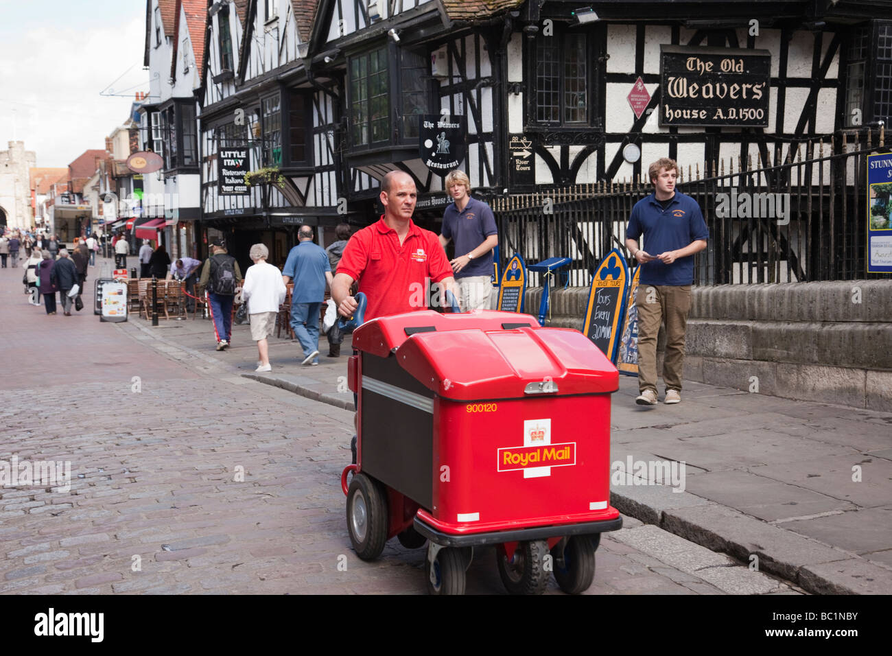 Un postino spingendo un Royal Mail post carrello consegna la posta in una strada della citta'. Canterbury Kent England Regno Unito Gran Bretagna Foto Stock