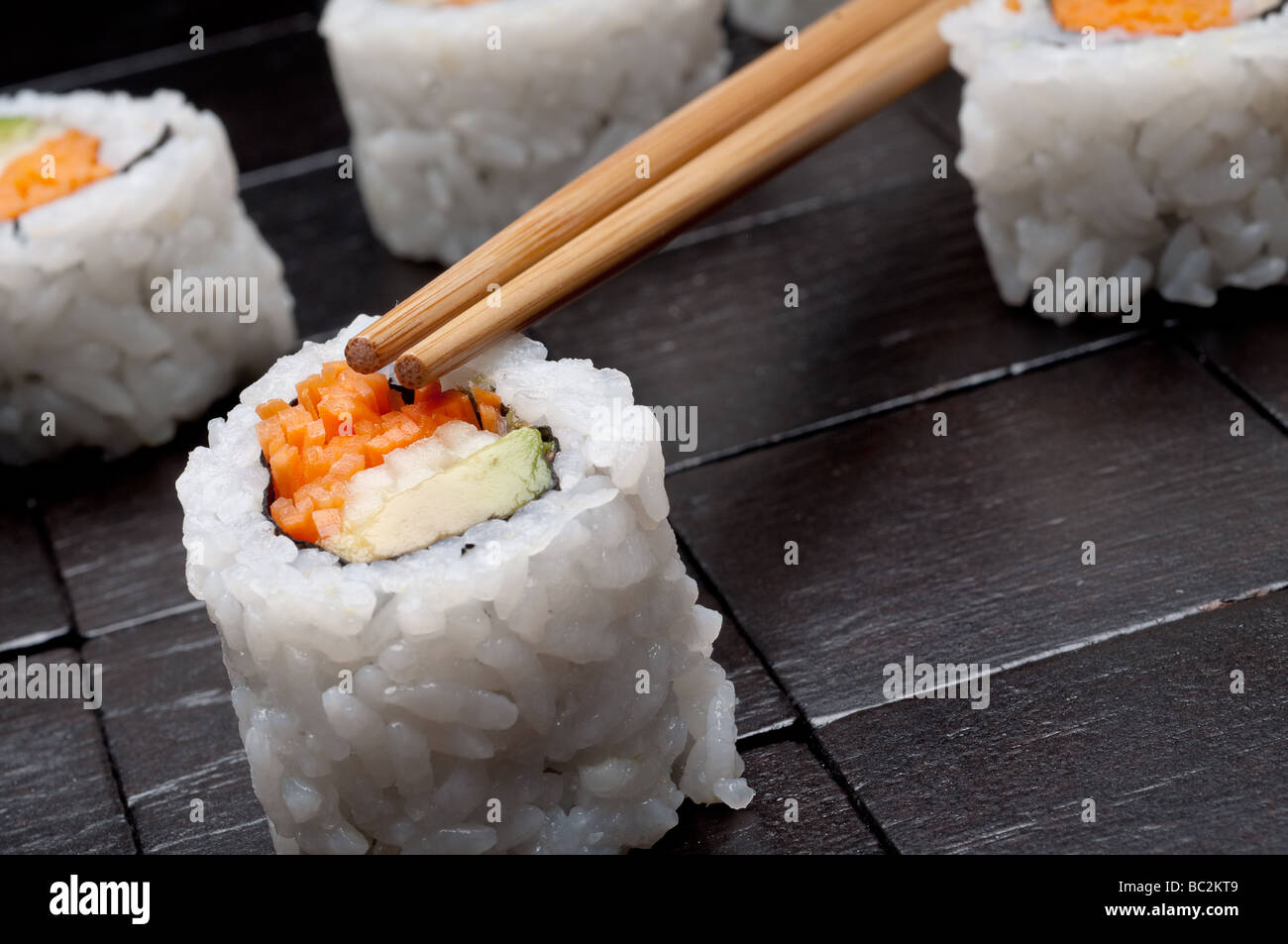 Un inclinato orizzontale poco profonda focus macro di sushi con copsticks su un nero lo sfondo di legno Foto Stock