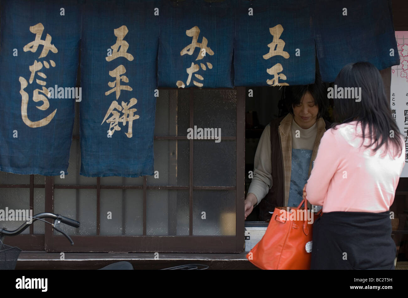 Una donna sta acquistando alcune specialità snack chiamato midarashi gohemochi da un quartiere merchant a Takayama Foto Stock