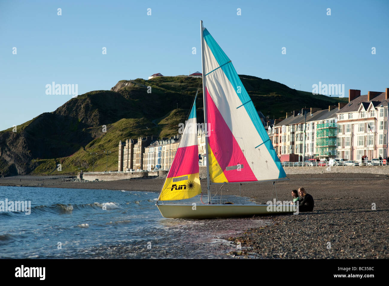 Serata estiva due persone con la loro piccola barca a vela dinghy sulla spiaggia Aberystwyth Wales UK Foto Stock