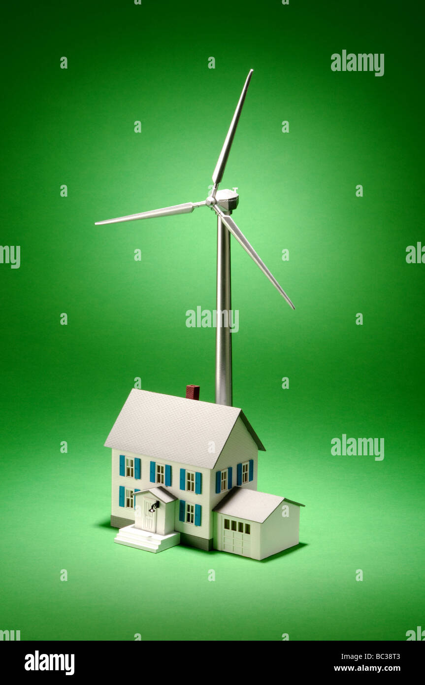Un piccolo oggetto metallico turbina eolica su uno sfondo verde con una piccola casa Foto Stock