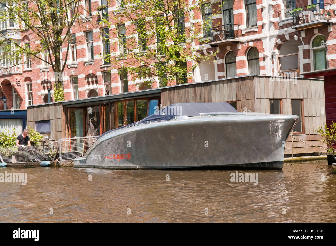 Grande, metallo speedboat, ormeggiata accanto a una casa galleggiante su un canale di Amsterdam Foto Stock
