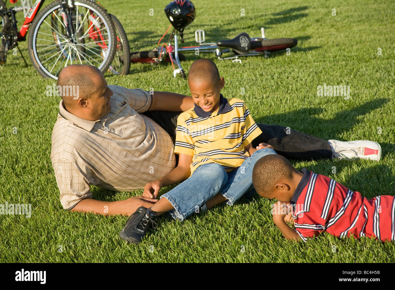 Papà ragazzi giovane persone padre figli a parlare il parlare l uno con l altro al di fuori di erba rilassante equitazione biciclette conversazione 5-9 anni anno di età Foto Stock