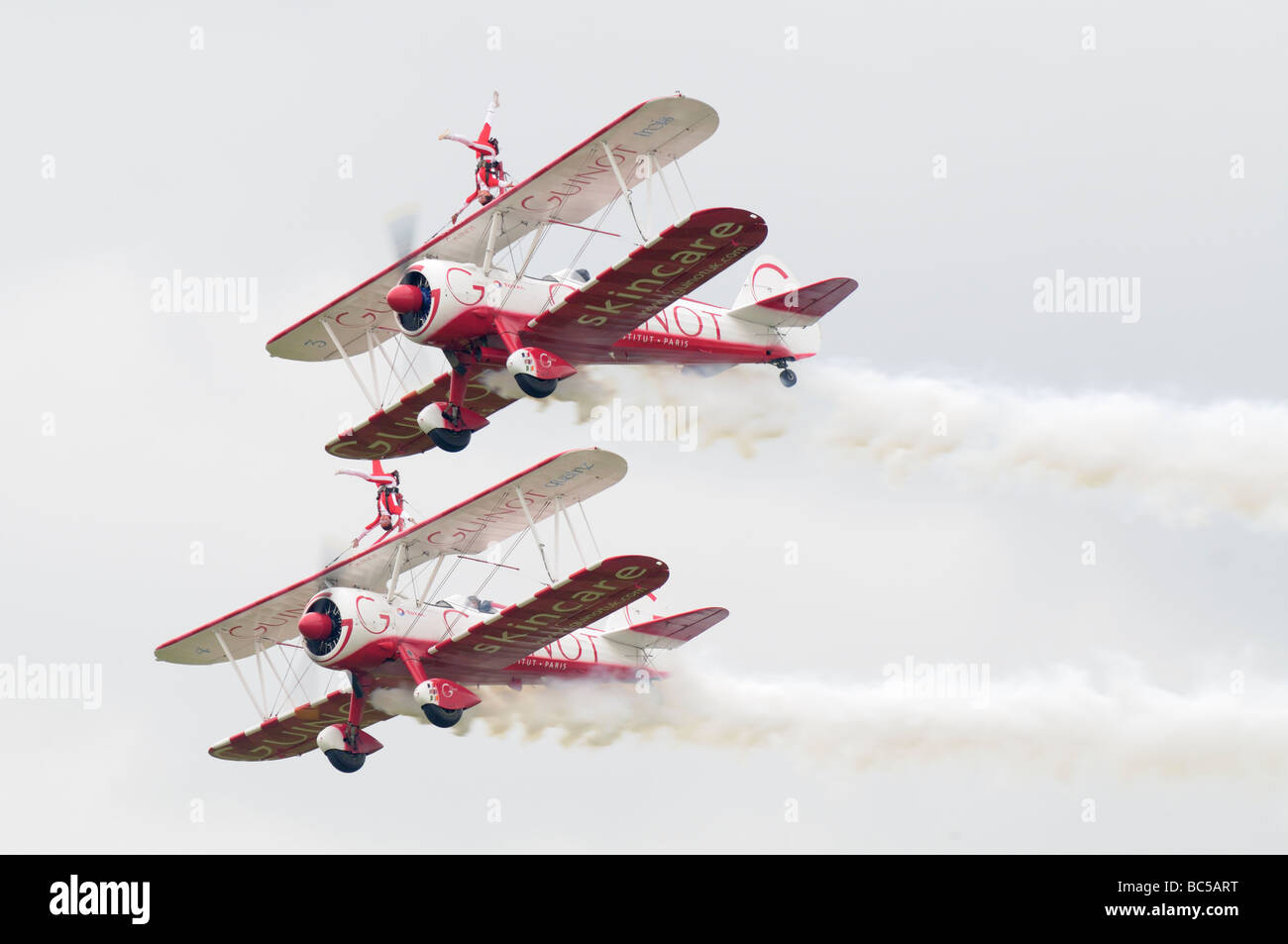 Due barnstorming biplani volare oltre in formazione con due giovani donne in piedi capovolto sull'ala. Foto Stock