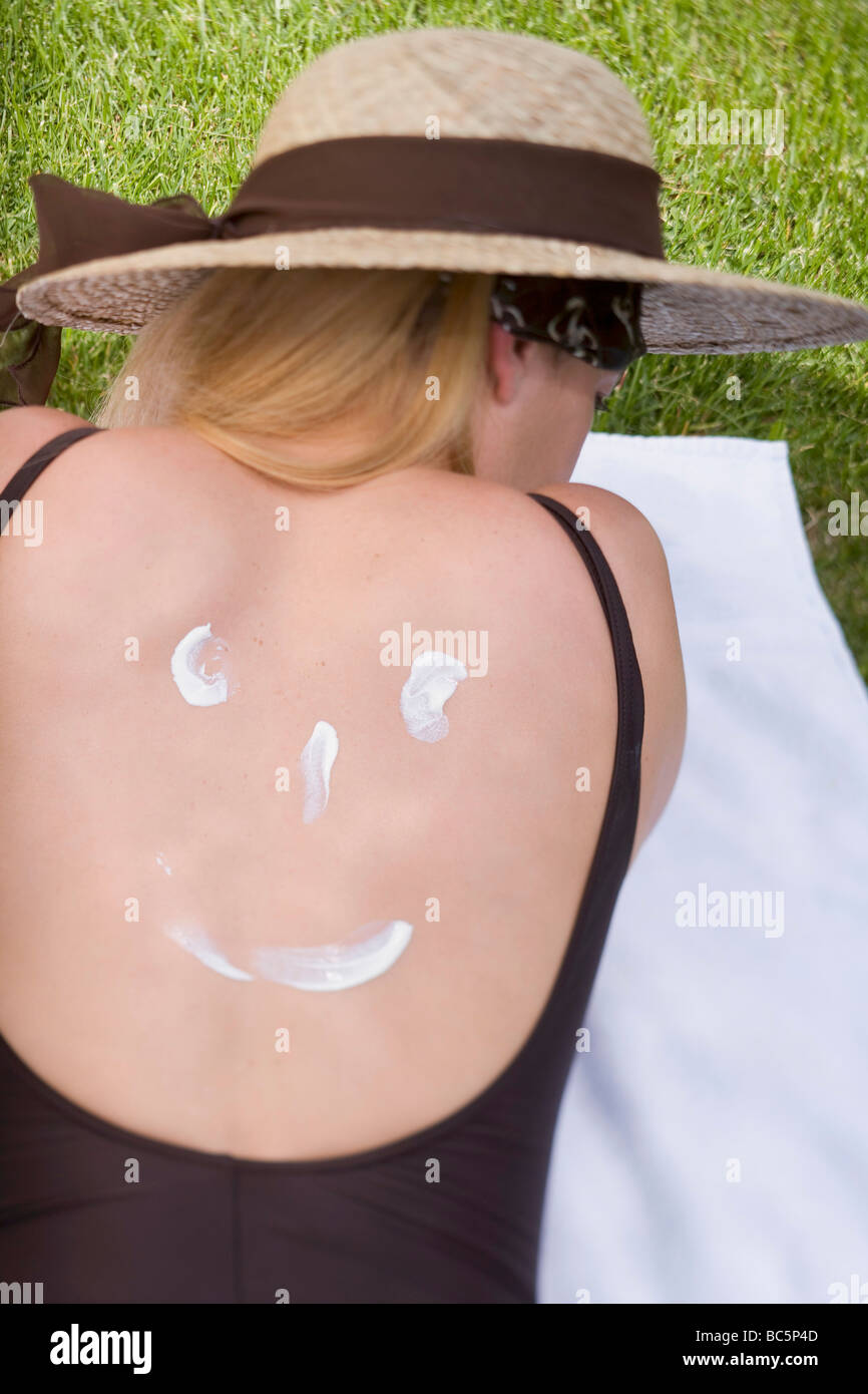 La donna nel cappello per il sole con crema solare sulla schiena - Foto Stock