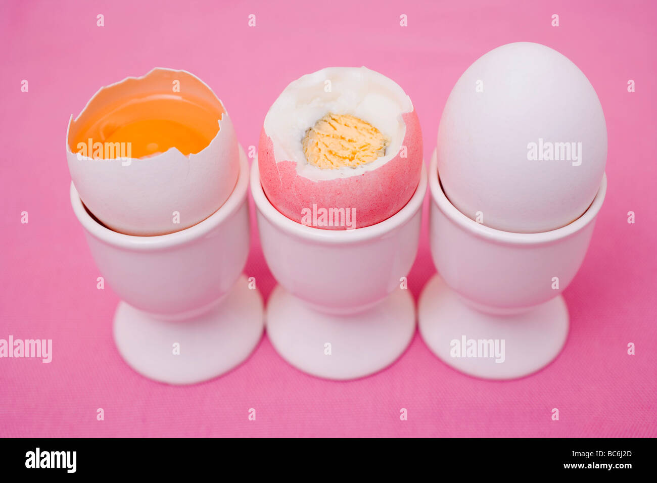 Tre uova in eggcups (raw e bollite con top cut off, intero) - Foto Stock