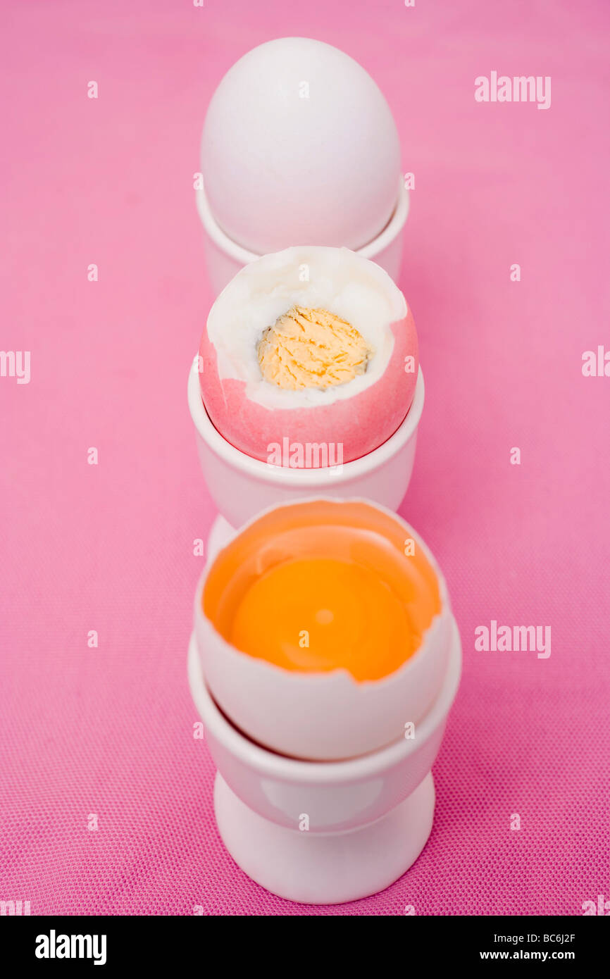 Tre uova in eggcups (raw e bollite con top cut off, intero) - Foto Stock