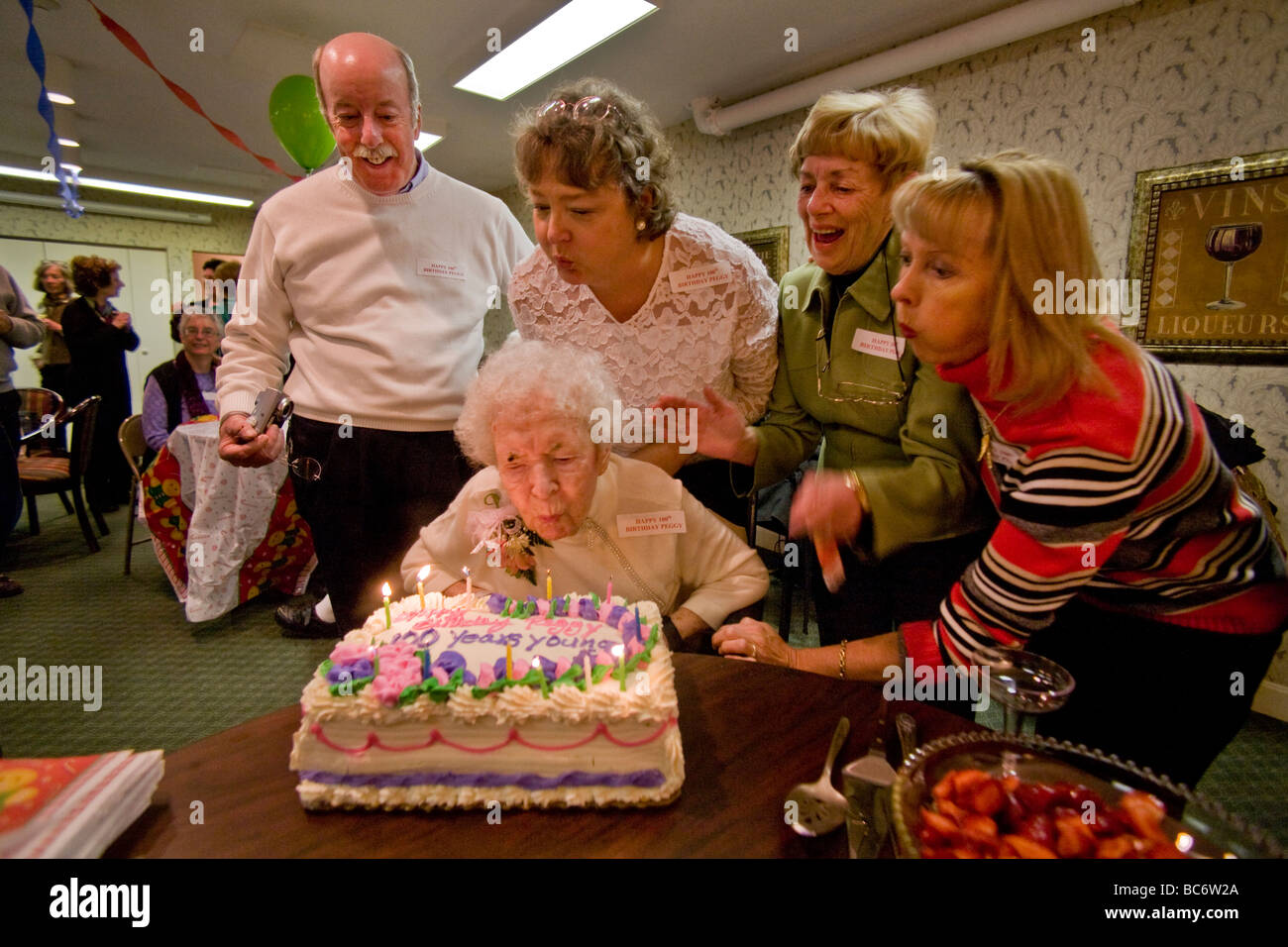 Assistito da familiari e amici un centenario si brucia le candele sulla sua torta durante il suo centesimo compleanno Foto Stock
