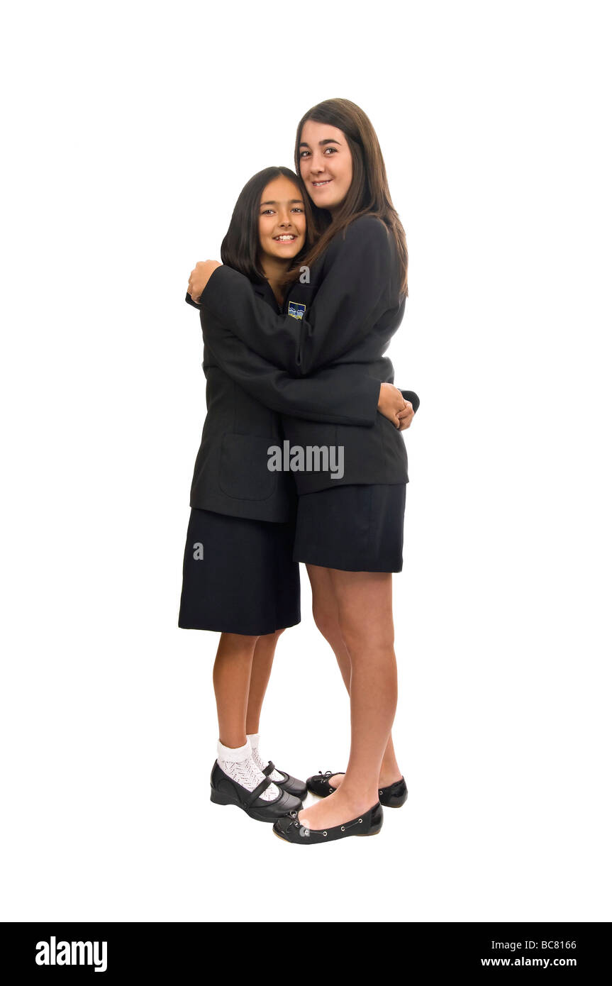 Chiudere verticale su ritratto di due sorelle adolescenti nelle loro uniformi di scuola che abbraccia ogni altra contro uno sfondo bianco Foto Stock