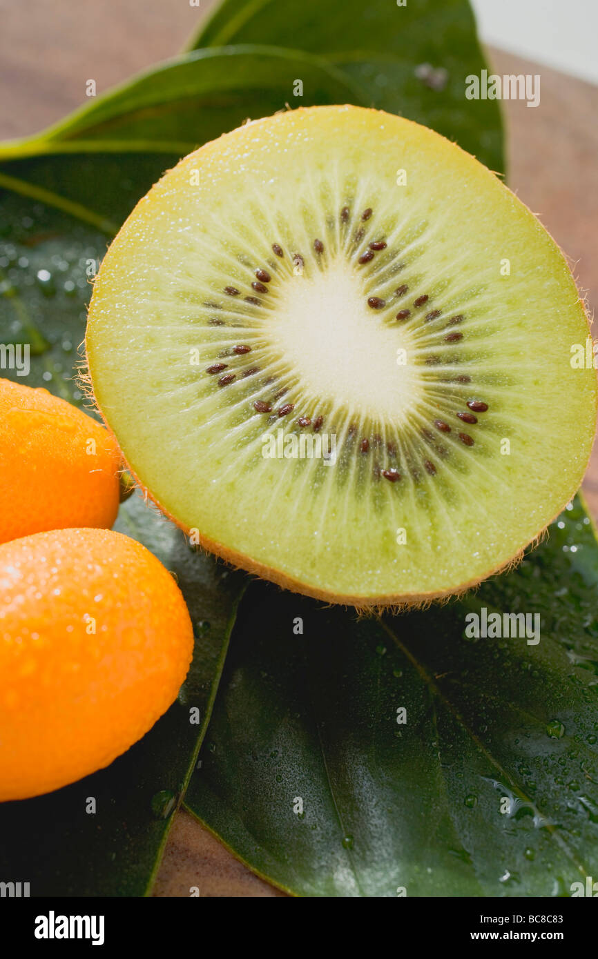 La metà di un kiwi e due kumquat su foglie - Foto Stock