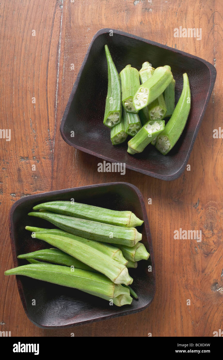 Diversi okra pods interi e tagliati in due, in due piatti - Foto Stock