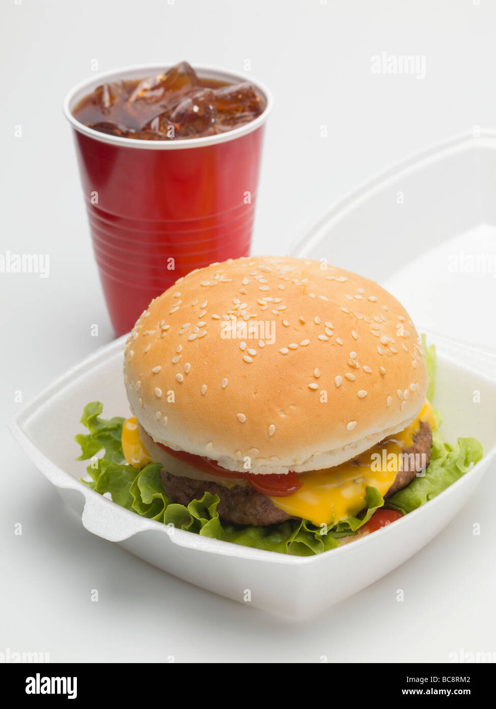 Cheeseburger in imballaggio, cola in una tazza di plastica - Foto Stock