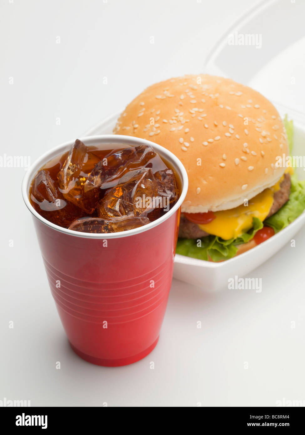 Cheeseburger in imballaggio, cola in una tazza di plastica - Foto Stock