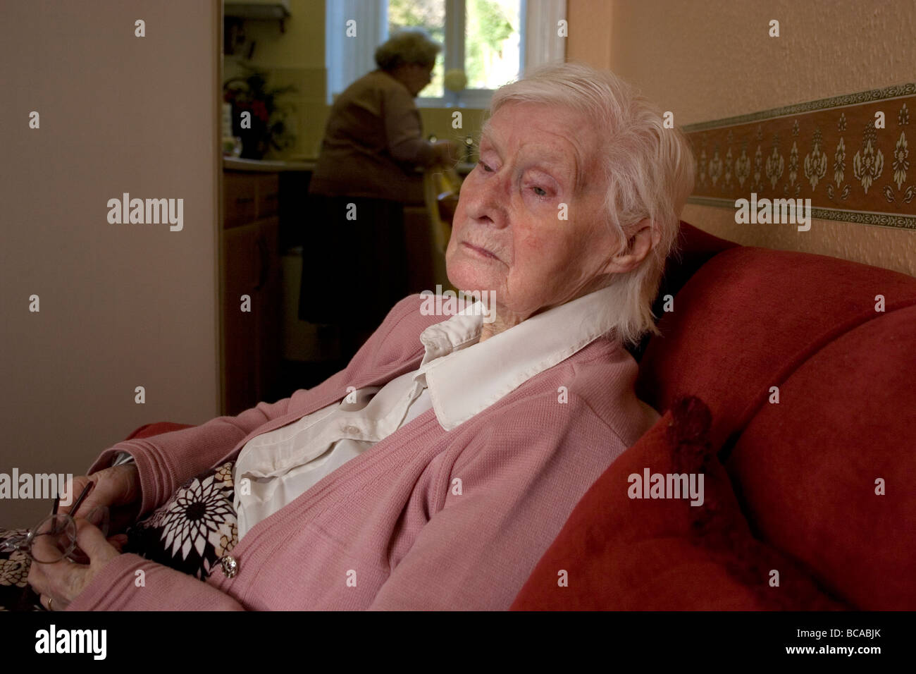 Infelice signora anziana seduti in poltrona a casa con un amico in cucina Foto Stock
