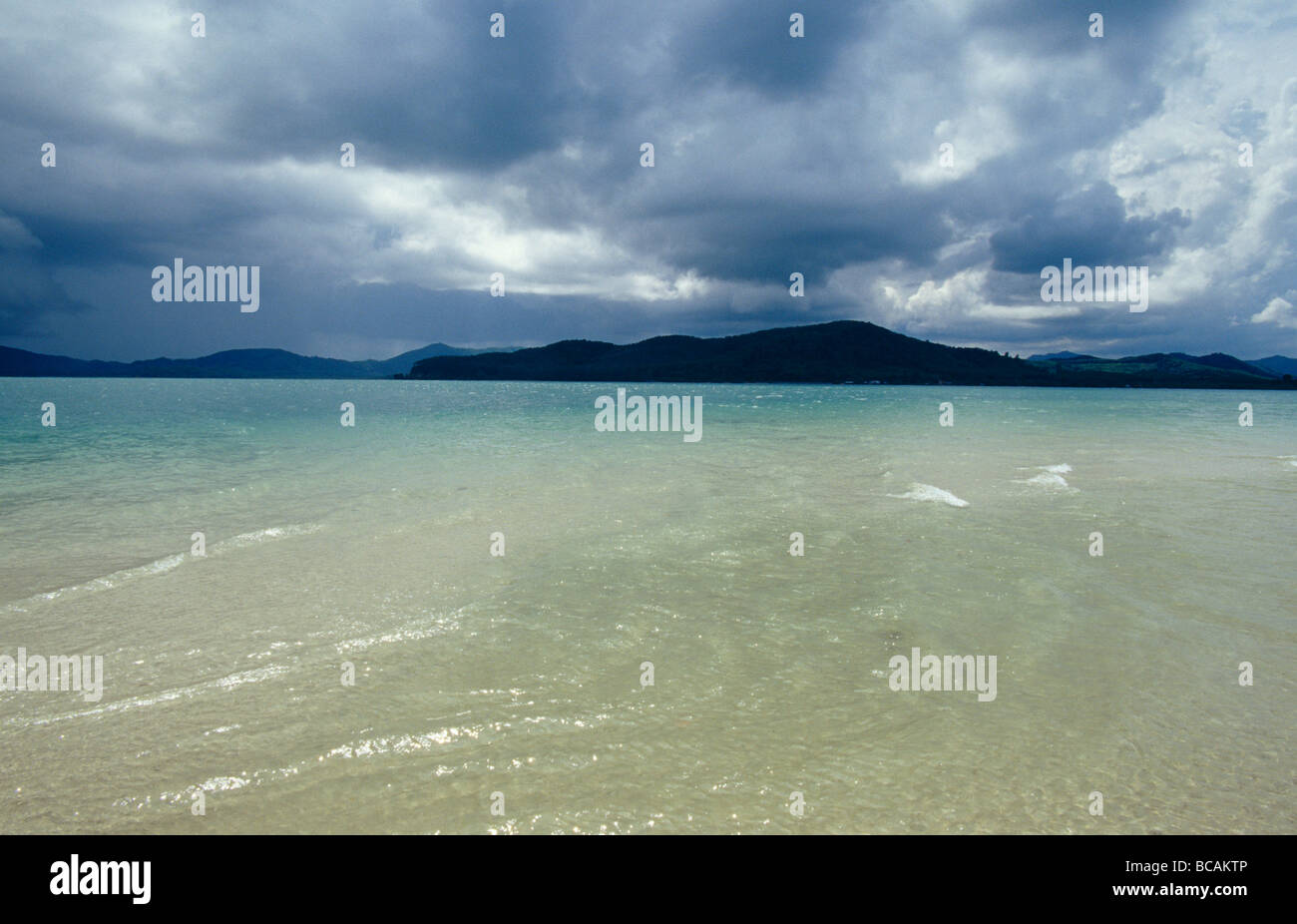 Limpide acque blu giro di una spiaggia di sabbia bianca davanti a nuvole temporalesche. Foto Stock