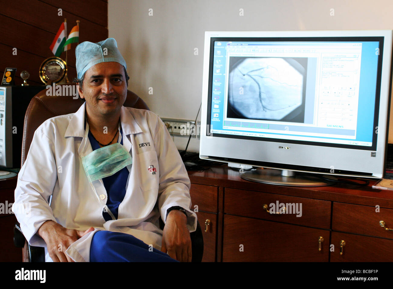 Il dr. Devi Shetty si siede di fronte a un monitor ad alta definizione che mostra parte di un paziente. Questo è un esempio di telemedicina. Foto Stock