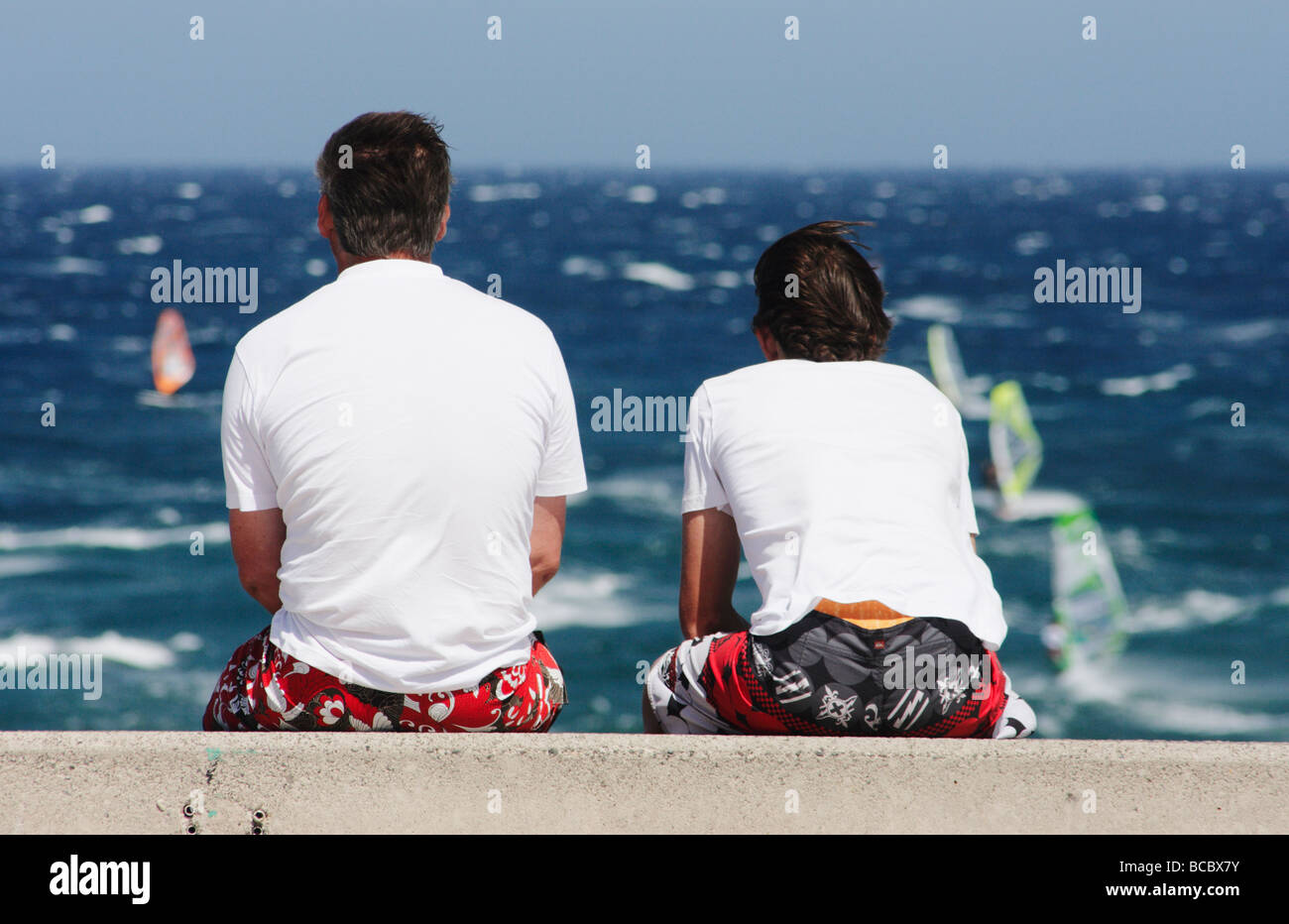 Due persone sedute sulla parete guardando windsurfisti del Pozo Izquierdo a Gran Canaria nelle Isole Canarie Foto Stock