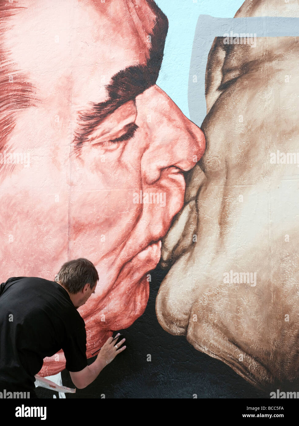 Artista russo Dimitry Vrubel ridipinge il suo famoso murale originale di Brezhnev kissing Honecker sul muro di Berlino Giugno Foto Stock