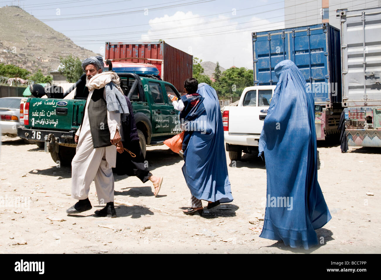 Attraversare una strada di Kabul, una famiglia comprese le donne a nascondere burqas, i rischi del traffico pericolosi Foto Stock