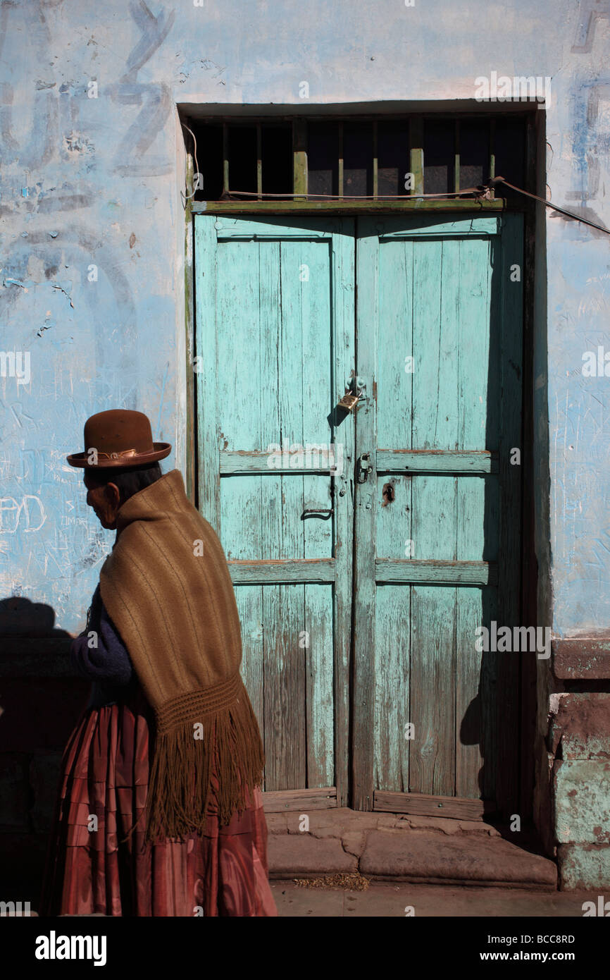 L Aymara signora in abito tradizionale a piedi passato porta rustico nel villaggio di Guaqui vicino a La Paz in Bolivia Foto Stock