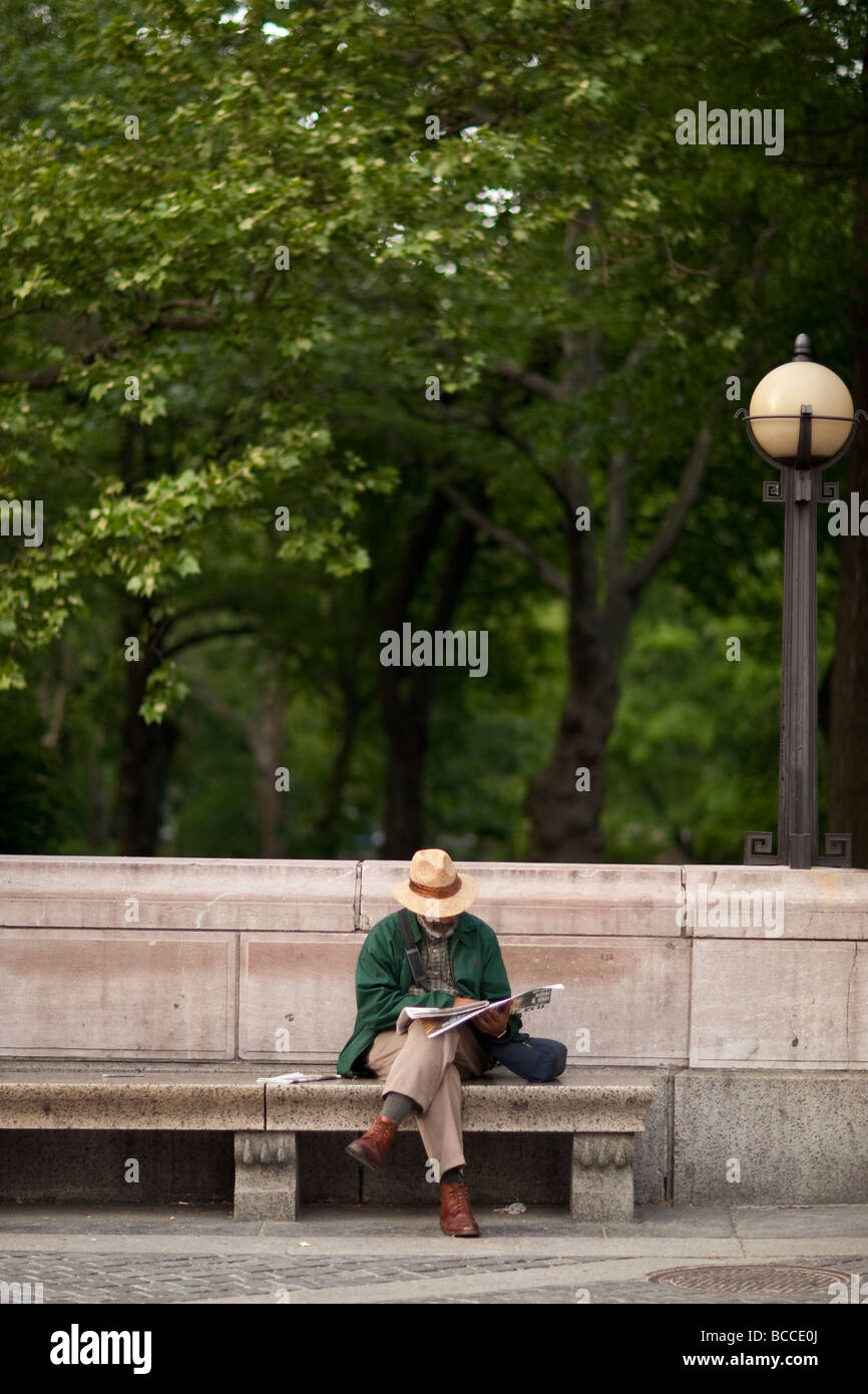 Uomo nero si siede su un banco di pietra da un parco e si legge il giornale in New York USA Maggio 2009 Foto Stock