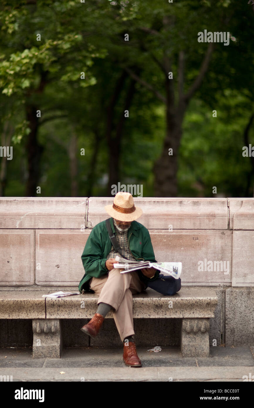 Uomo nero si siede su un banco di pietra da un parco e si legge il giornale in New York USA Maggio 2009 Foto Stock