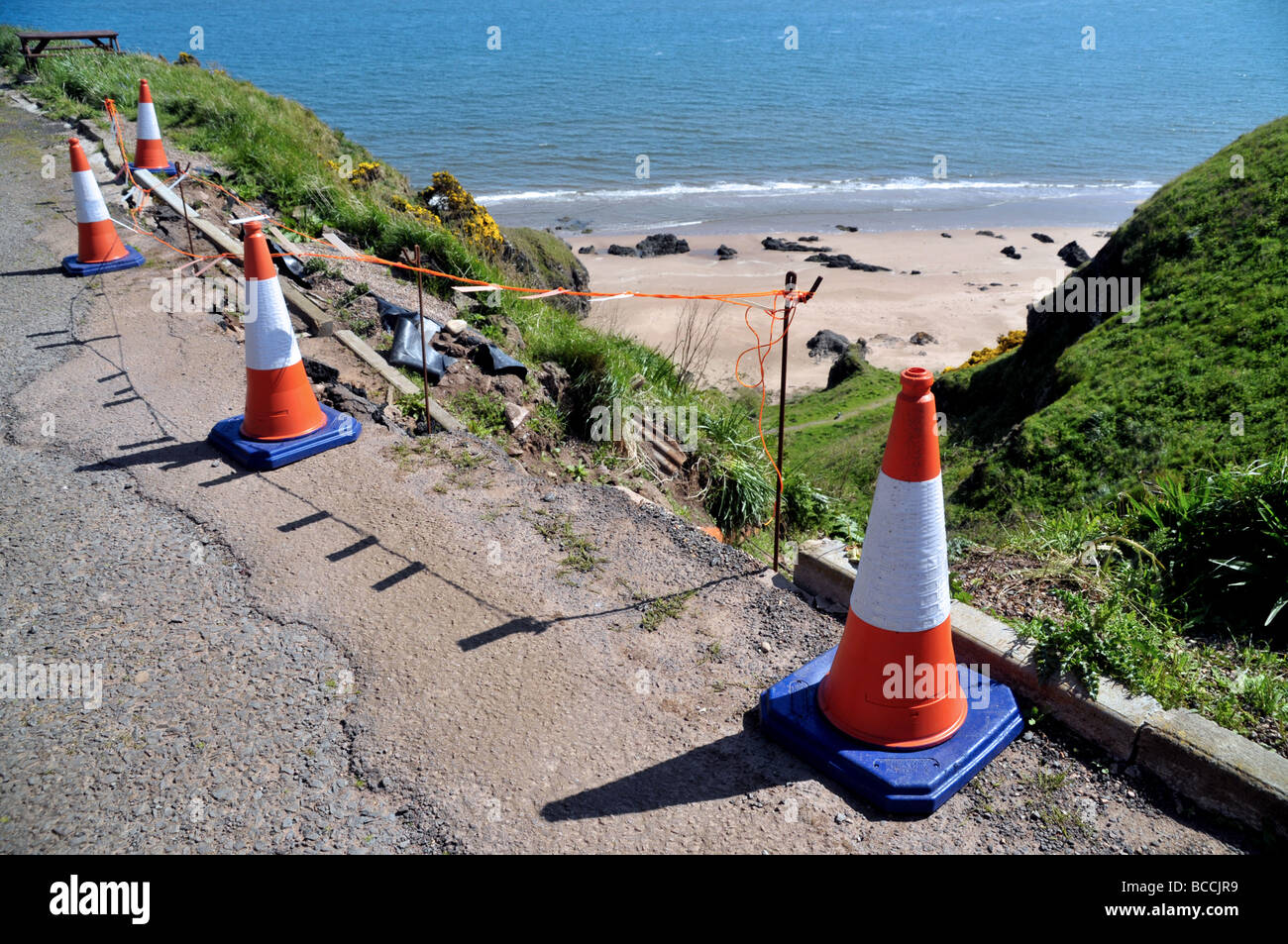 Traffico coni e nastro di pericolo a sigillare il bordo di un erodendo la strada costiera. Foto Stock