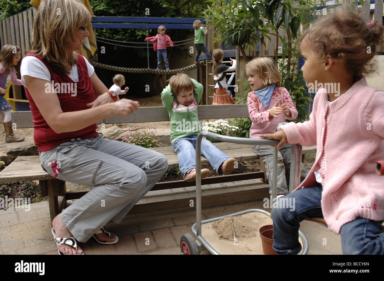 I bambini e il maestro giocando su un parco giochi in un asilo nido su un giorno d'estate. Foto Stock