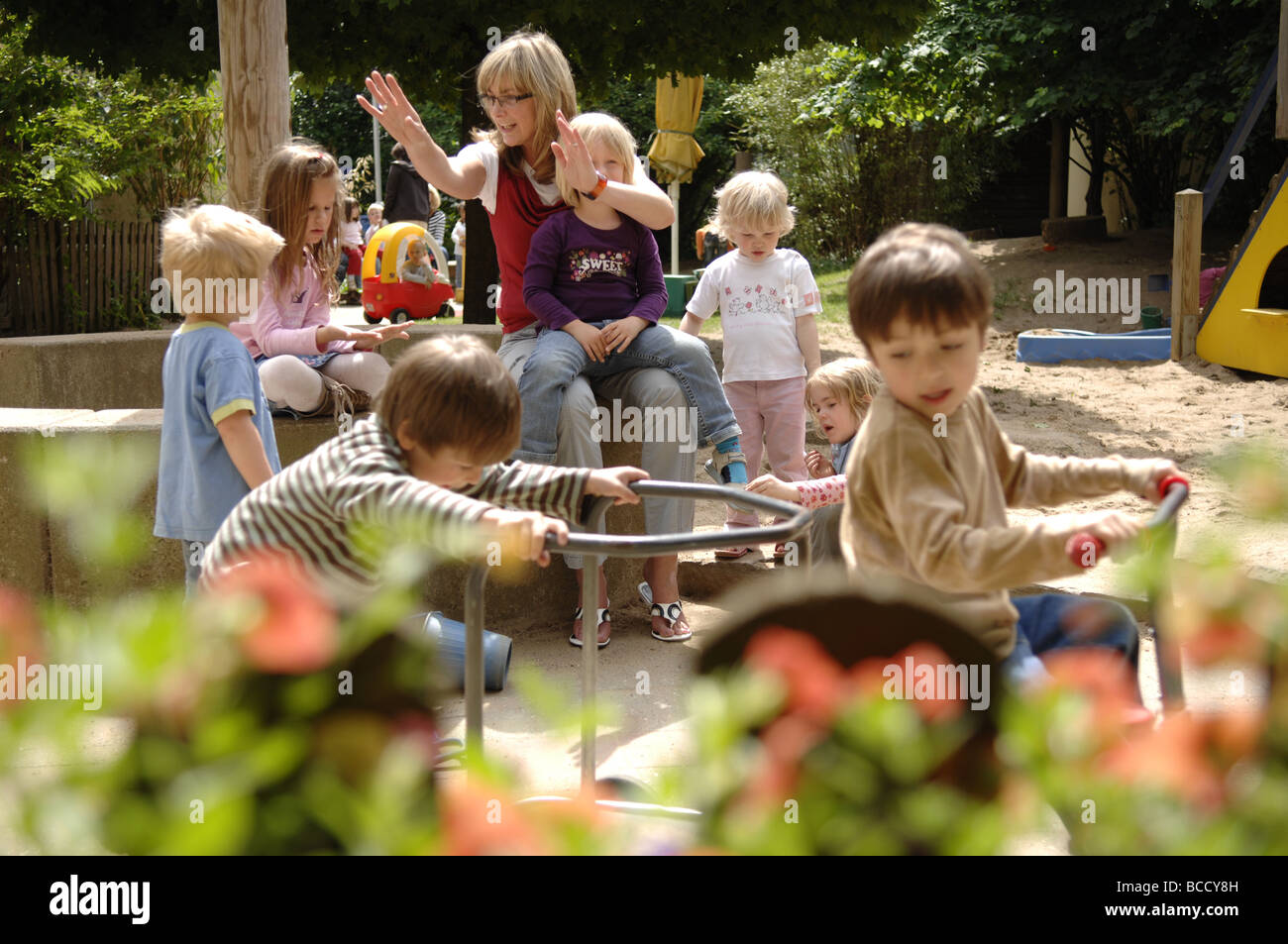 I bambini e il maestro giocando su un parco giochi in un asilo nido su un giorno d'estate. Foto Stock