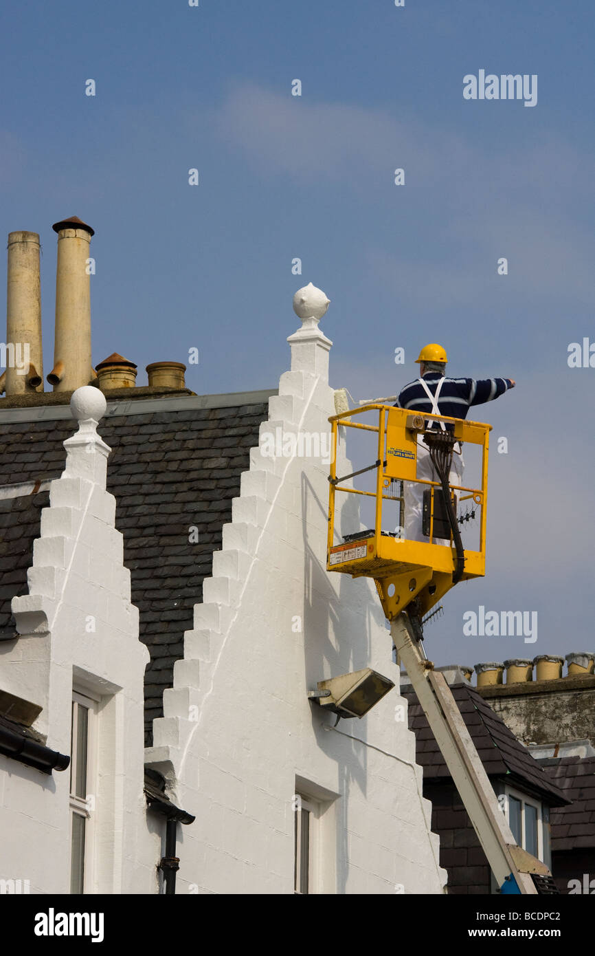 Casa pittura utilizzando 'cherry picker' o di sollevamento telescopico a Portree, Isola di Skye, Scotland, Regno Unito Foto Stock