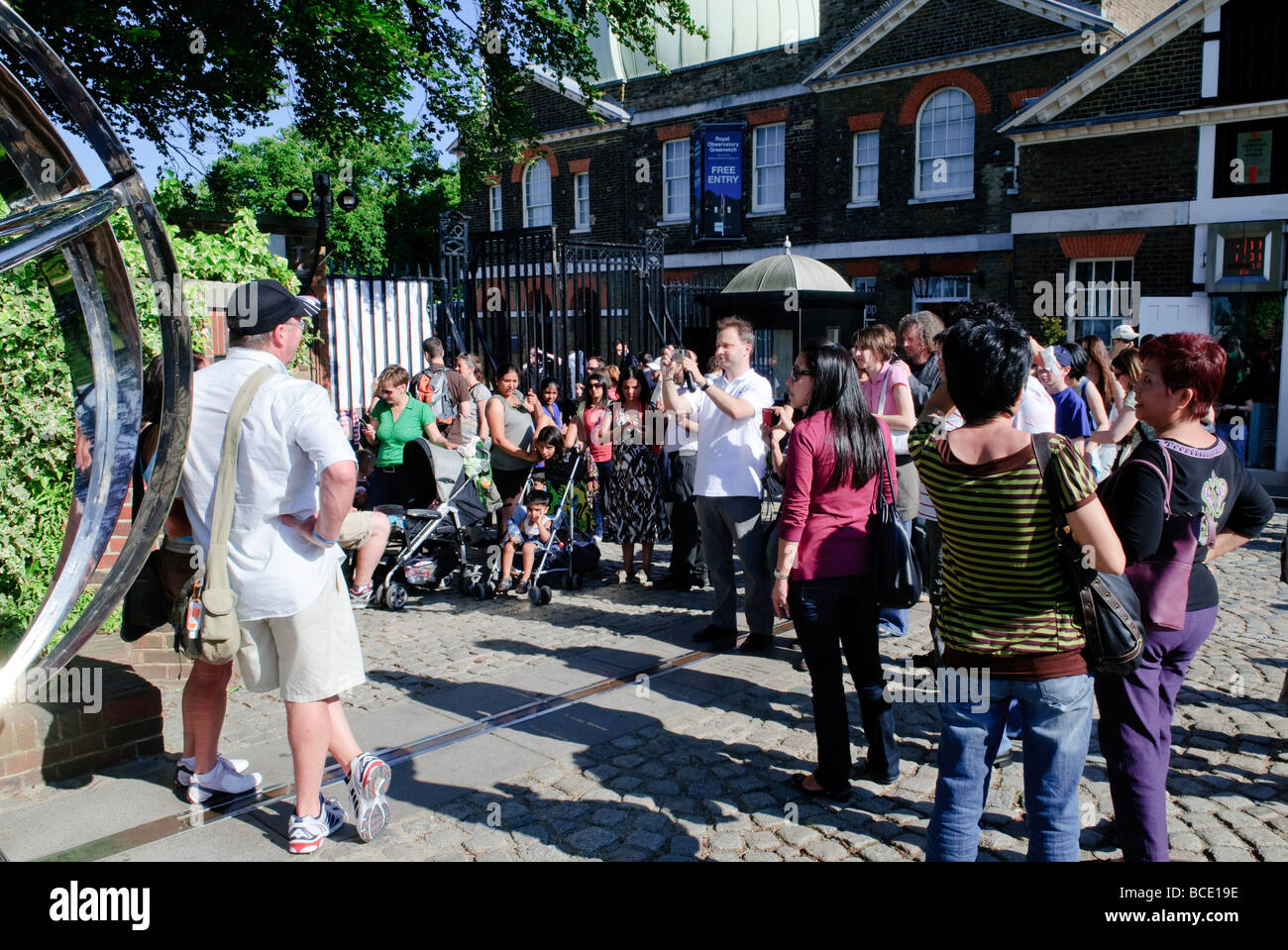 Prime Meridian Line Tourists Royal Observatory Greenwich Londra // LONDRA, Regno Unito - i turisti si riuniscono per posare per le fotografie sulla linea prime Meridian fuori dal Royal Observatory di Greenwich. Questa striscia di ottone nel cortile rappresenta 0° di longitudine, il punto di partenza riconosciuto a livello mondiale per misurare le distanze est-ovest. I visitatori possono essere visti a cavallo della linea, simbolicamente in piedi sia nell'emisfero orientale che nell'emisfero occidentale contemporaneamente, catturando un'opportunità fotografica popolare in questo significativo punto di riferimento geografico e storico. Foto Stock
