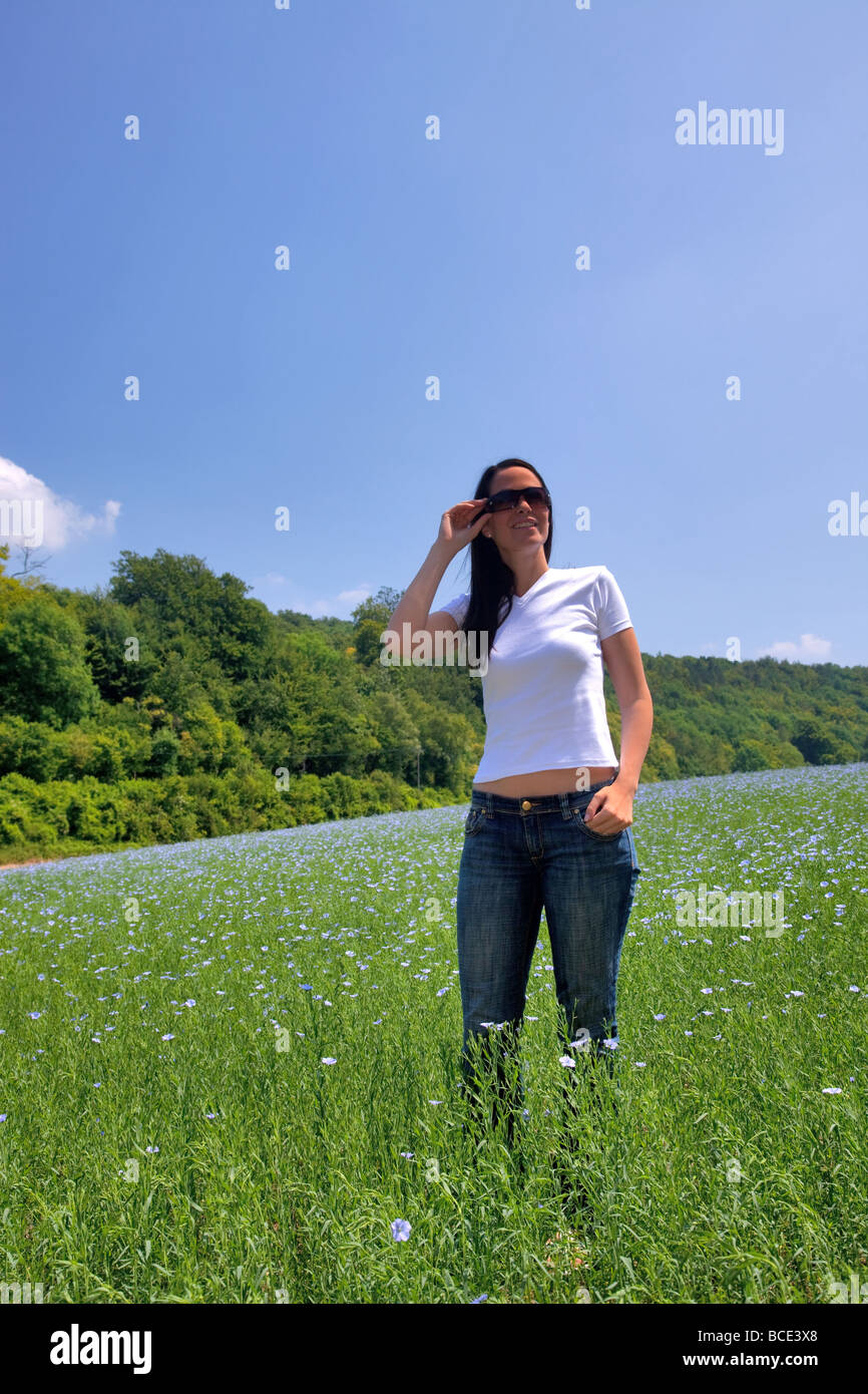 Bella bruna donna in un campo di fiori blu in una giornata di sole Foto Stock