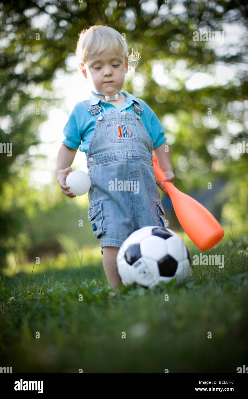 Il Toddler giocando in esterni con una mazza da baseball e pallone da calcio Foto Stock