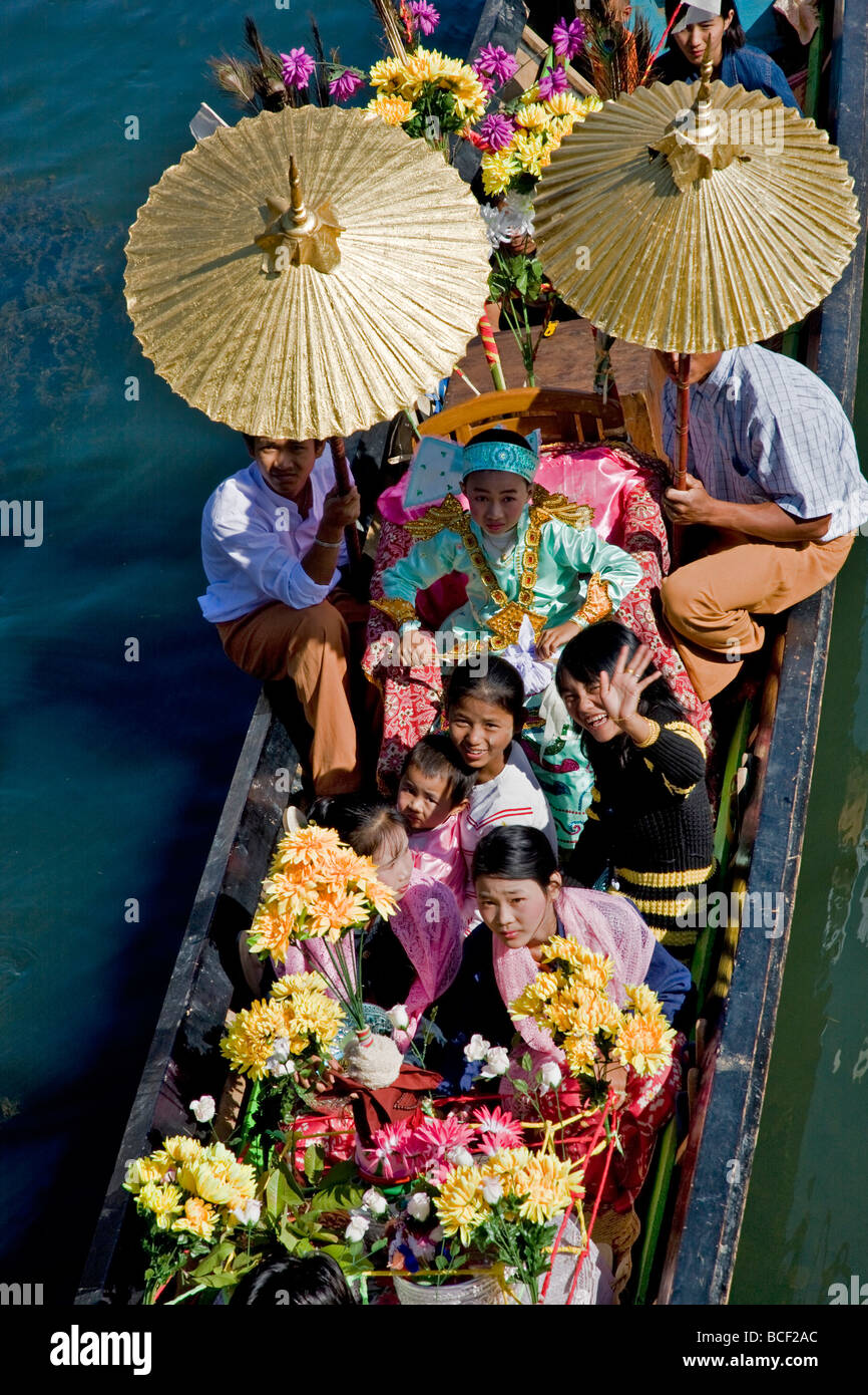 Myanmar Birmania, Lago Inle. Un giovane noviziato ombreggiata con golden ombrelloni viaggi in barca durante una cerimonia. Foto Stock
