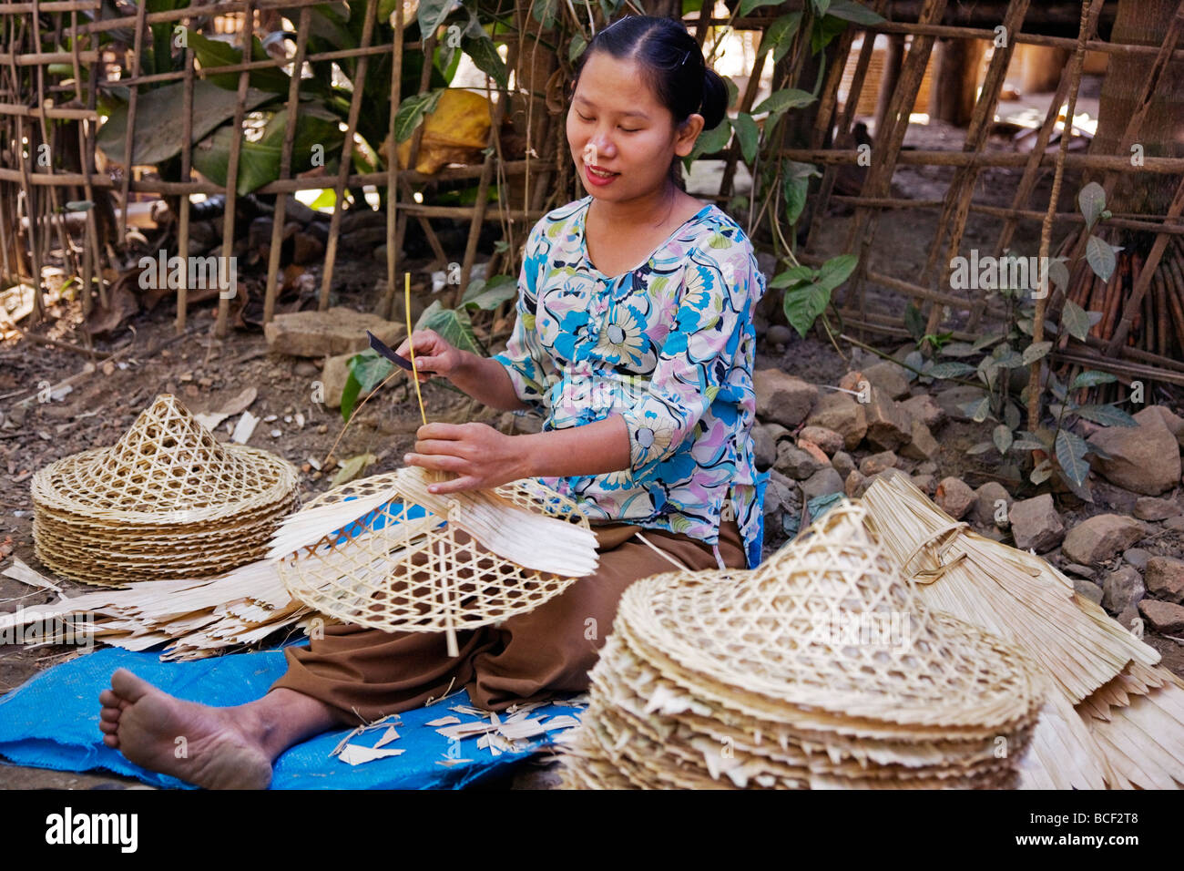 Myanmar Birmania Mrauk U. Una donna si applica abilmente guaine di bambù per la cornice di bambù di una conica, largo-colmato hat. Foto Stock