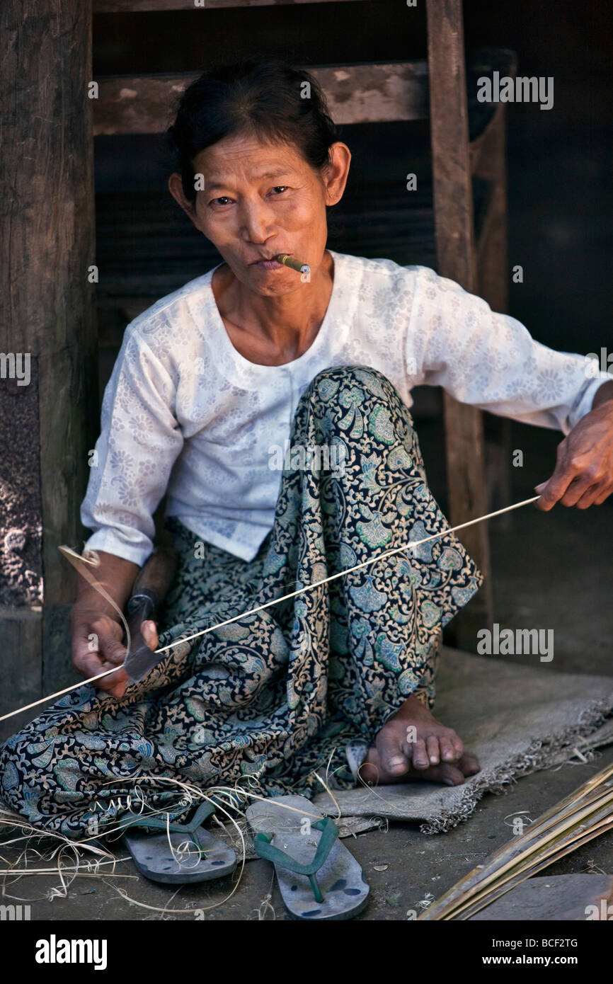 Myanmar Birmania Mrauk U. Una donna Rakhine fuma una cheroot come lei divide il bambù per fare una vasta-colmato, bambù hat. Foto Stock